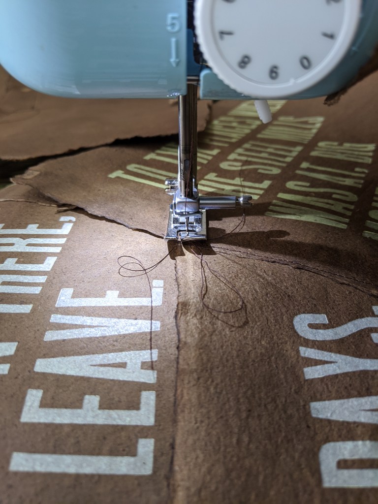 Close-up of a sewing machine stitching pieces of letterpress-printed paper.