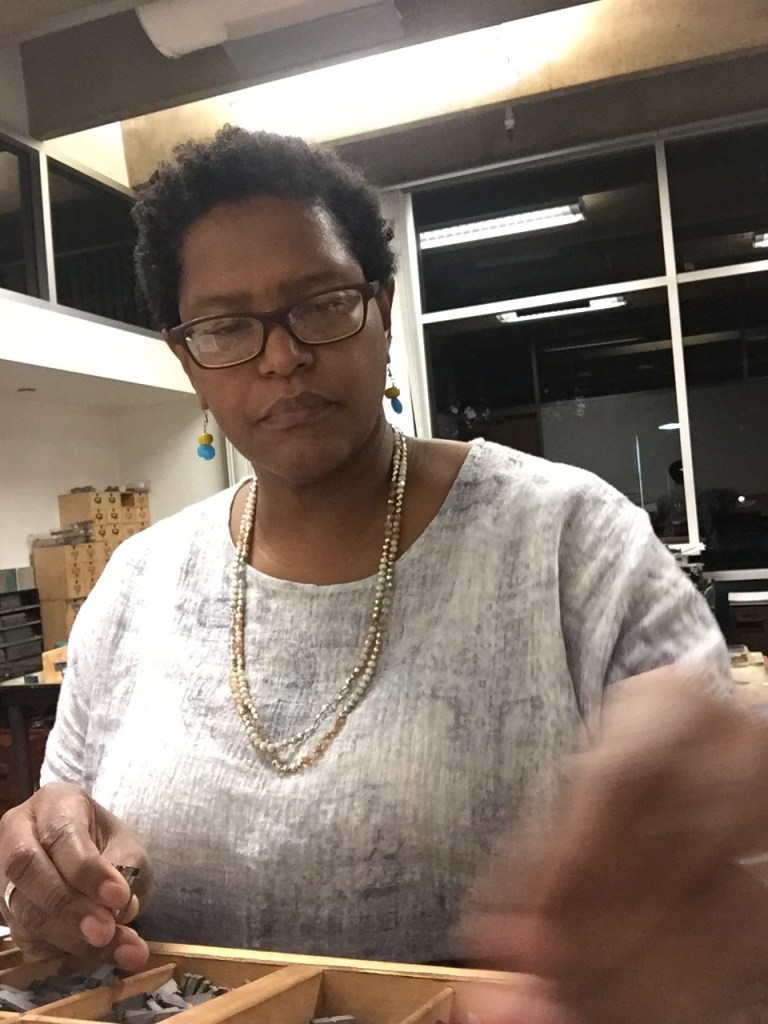 Portrait of Tia Blassingame setting metal type from a job case, working on the book, "I AM".