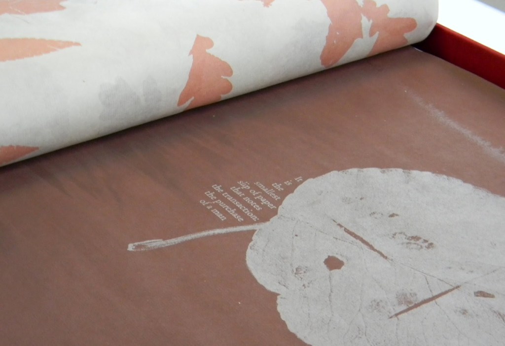 Close-up of a page from "Harvest: Holding & Trading" depicts a screen-printed leaf and text in white on a brown page. 