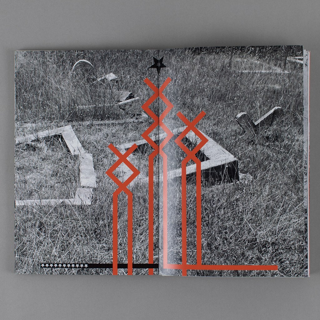 This Land is My Land, inside opening from early in the book. A black and white photo of a neglected cemetery spans the full spread. Red, abstract symbols based on the "othala rune" are centered in the composition, with black and white stars at the top and bottom left