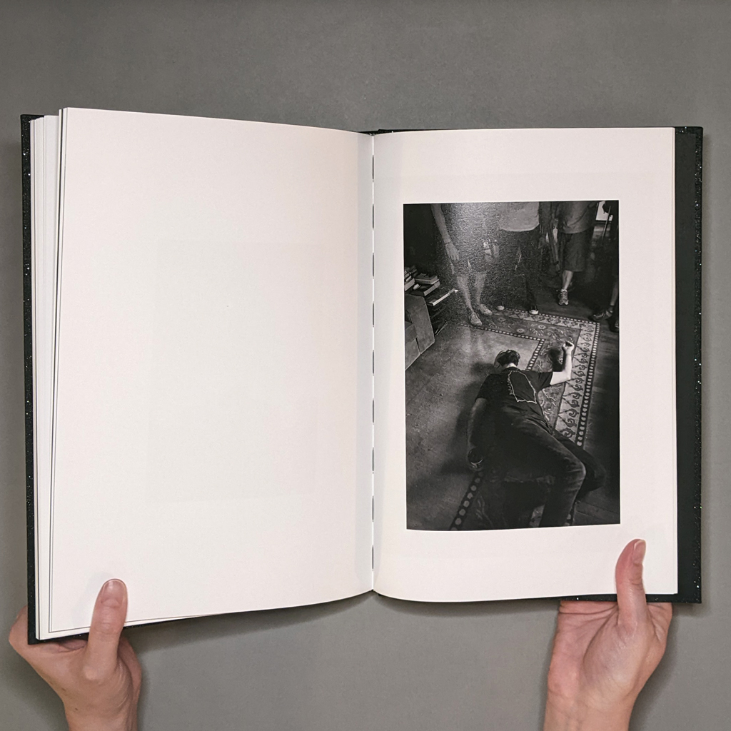 A Ghost Story: Photographs, inside spread. Verso is blank. Recto shows a black and white photo of a man playing dead on the floor, wearing a T-shirt printed with the book's cover image.