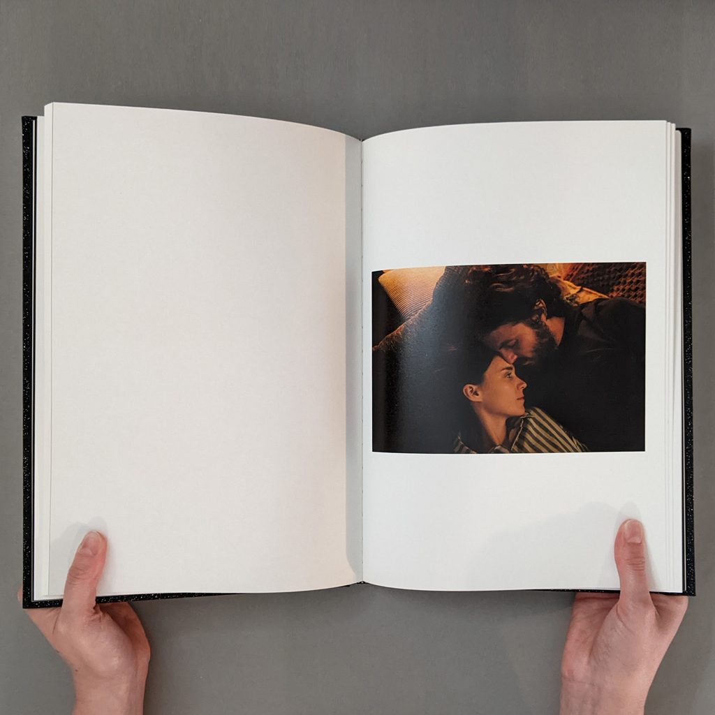 A Ghost Story: Photographs, inside spread. Verso is blank. Recto shows a warm-toned close-up photograph of a couple cuddling.